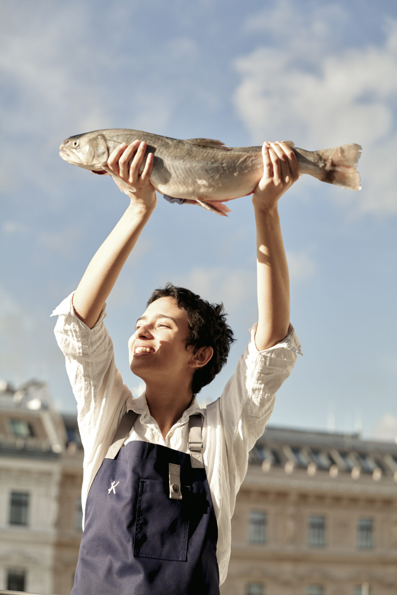 Eine angestellte des Kelsen hält lächelnd einen Fisch über ihren Kopf